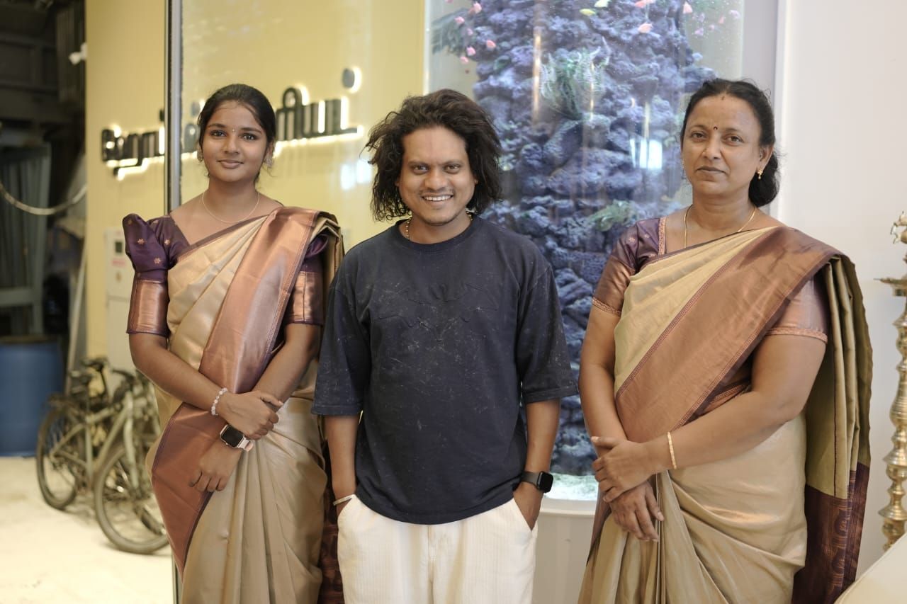 Three individuals standing in a room with a Christmas tree in the background.