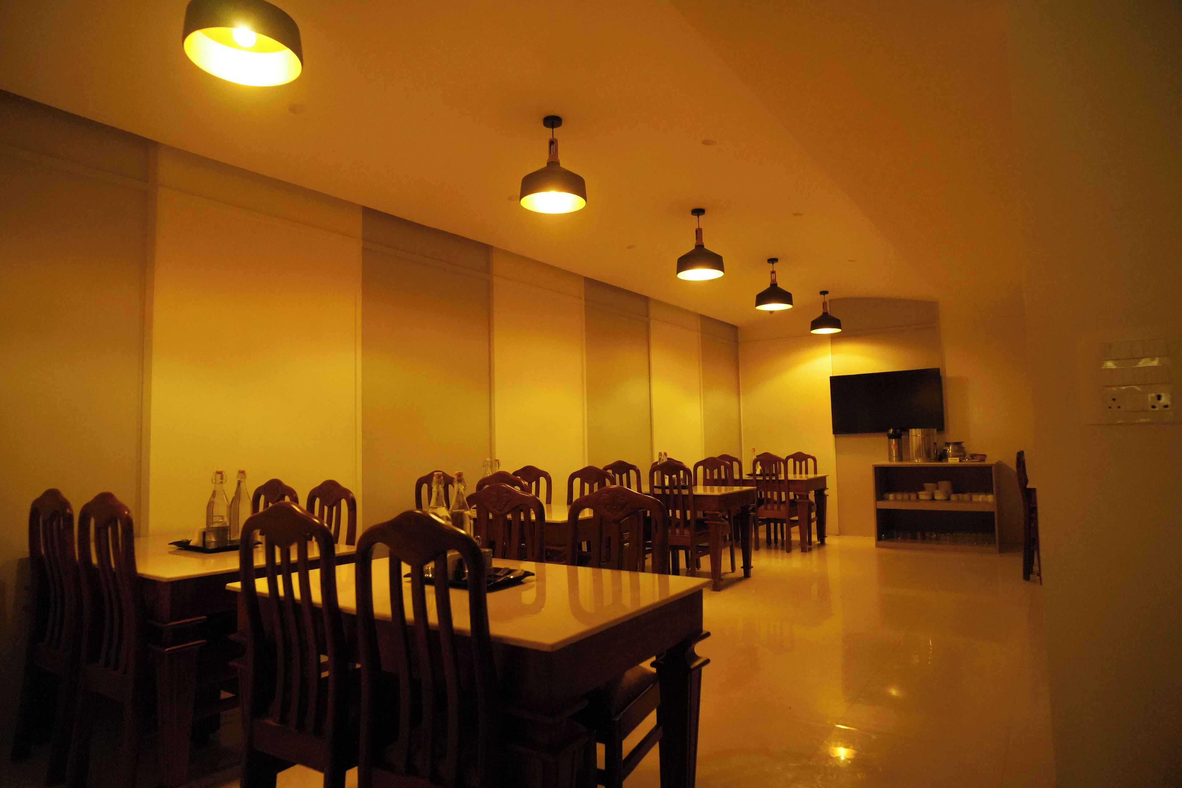 A dining area with multiple tables and chairs, a flat-screen TV mounted on the wall, and pendant lighting.