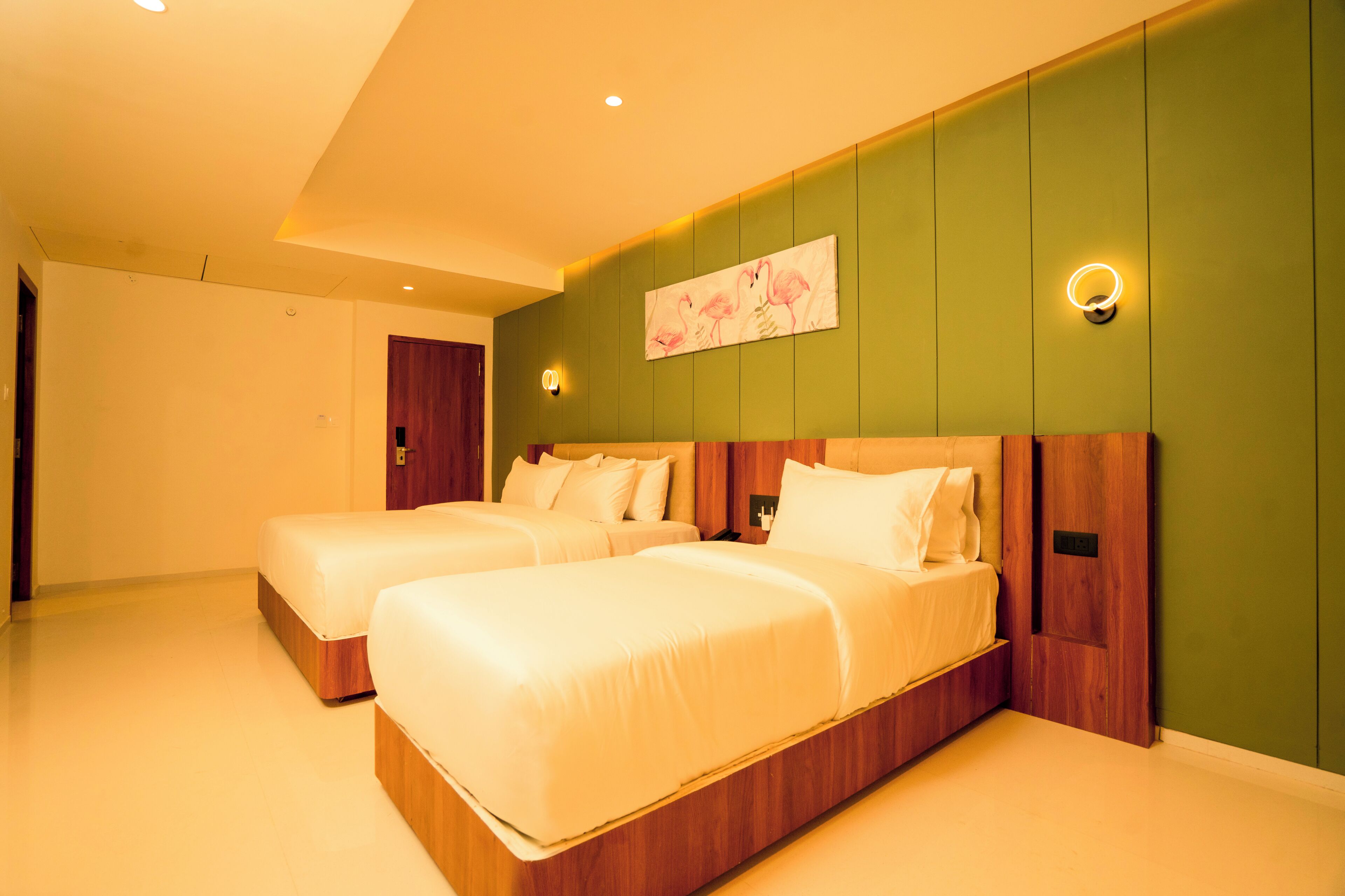 Une chambre d’hôtel avec deux lits, un mur d’accent de couleur verte et un tableau représentant des flamants roses.
