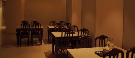 A dining area with tables and chairs, recessed ceiling lights, and a tiled floor.