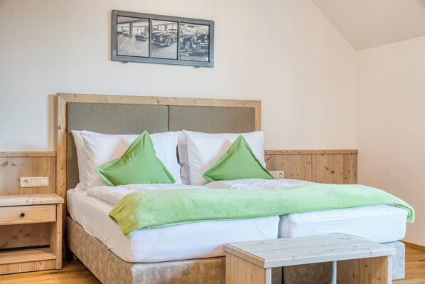 Una cama bien tendida con ropa de cama blanca y verde, un cabecero de madera y una mesita de noche pequeña.
