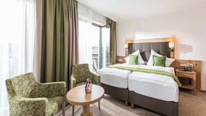Una habitación de hotel con una cama, dos sillones, una mesita y una mesita de noche.