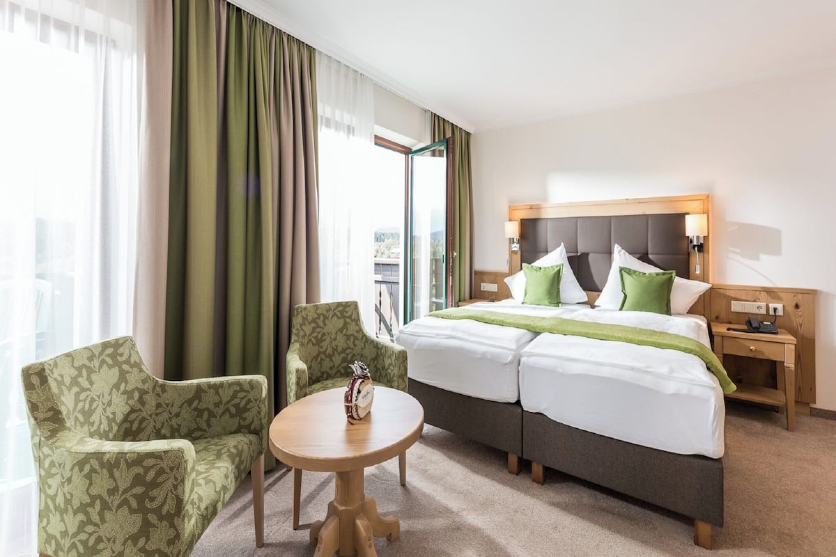 Una habitación de hotel con una cama, dos sillones, una mesita y una mesita de noche.