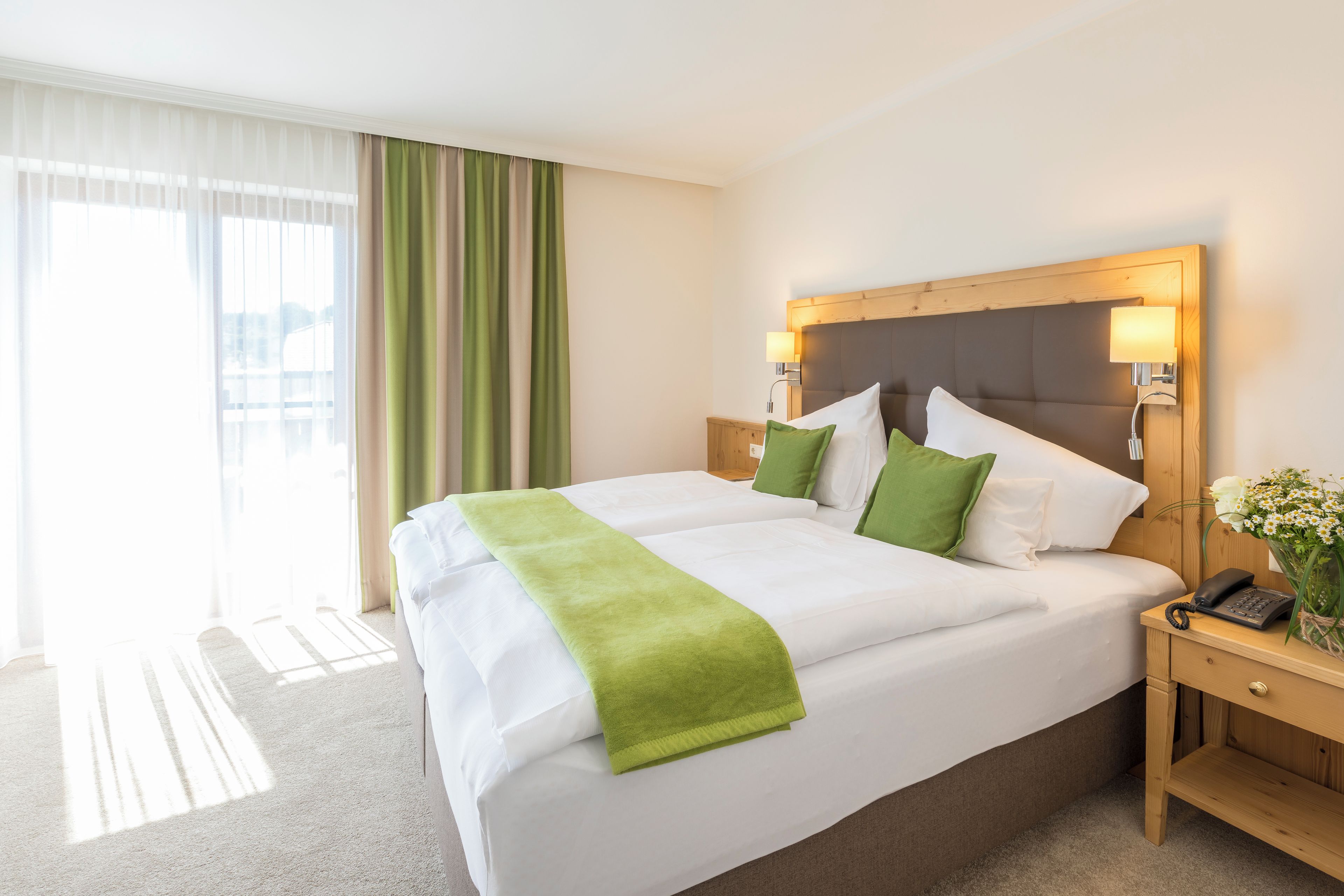 Een hotelkamer met een groot bed, twee nachtkastjes, een houten hoofdbord en een raam met gordijnen.
