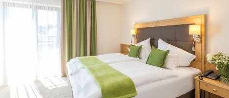 A hotel room with a large bed, two bedside tables, a wooden headboard, and a window with curtains.