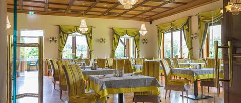 A dining area with multiple tables and chairs, wooden flooring, and green curtains.