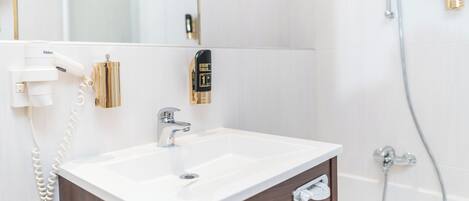 Un baño con un lavamanos blanco, un espejo, un secador de manos y una ducha.