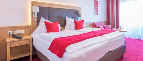 A hotel room with a large bed, a bedside table with a lamp, a phone, and a small table with a clock.