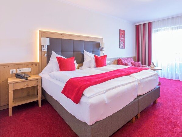 A hotel room with a large bed, a bedside table with a lamp, a phone, and a small table with a clock. - Marienhof Velden - Mein Refugium (Velden am Wörther See)