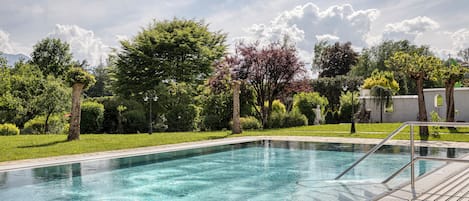 Una piscina cristalina con un muelle de madera y barandillas metálicas, rodeada de exuberante follaje y árboles.