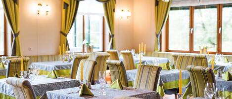A dining area with tables set for multiple guests, featuring striped chairs and green tablecloths.