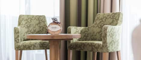 Una mesa redonda de madera con un reloj, flanqueada por dos sillas estampadas.
