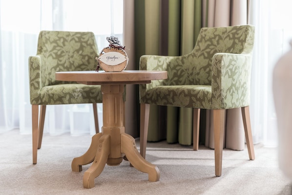 Una mesa redonda de madera con un reloj, flanqueada por dos sillas estampadas.