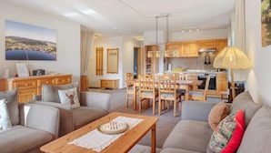 A modern living room with a sofa, a dining table, and a kitchen in the background. - Lotti Apartment with Mountain Views, Balcony, and Wi-Fi (Titisee-Neustadt)