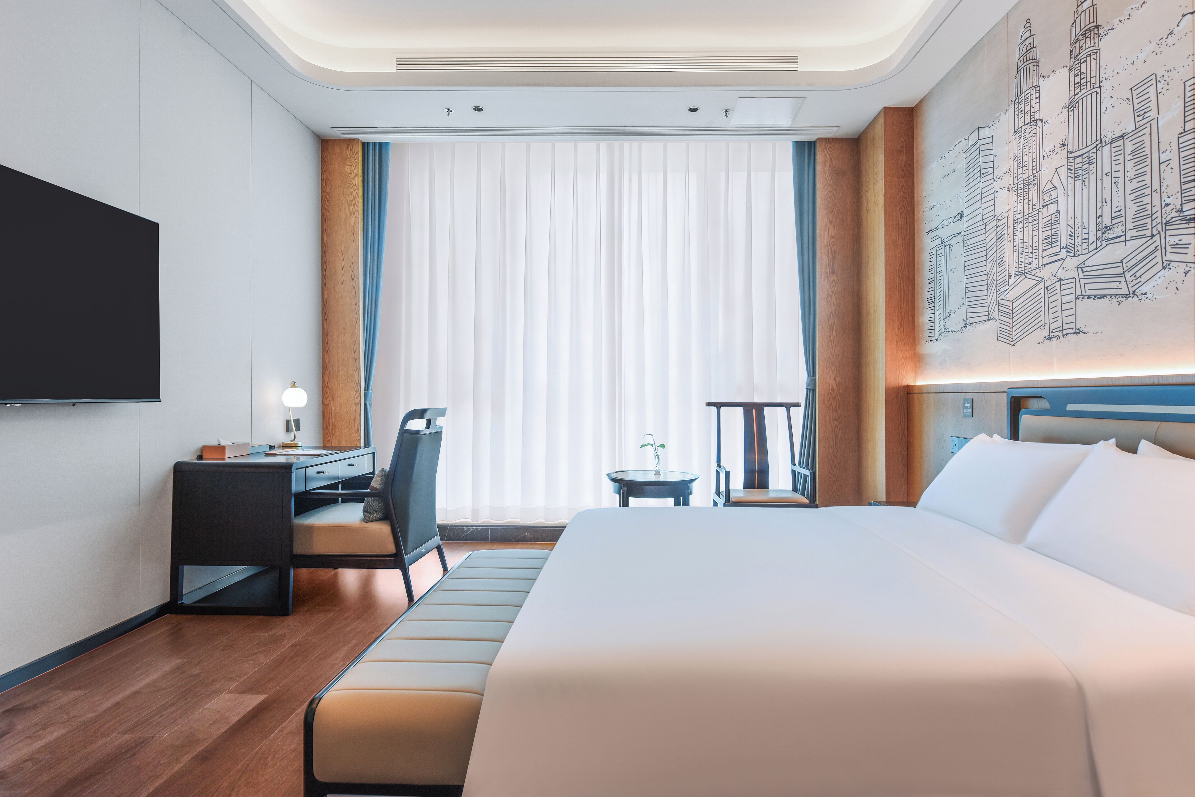 A modern hotel room with a large bed, a desk, a chair, a small table, and a TV mounted on the wall.