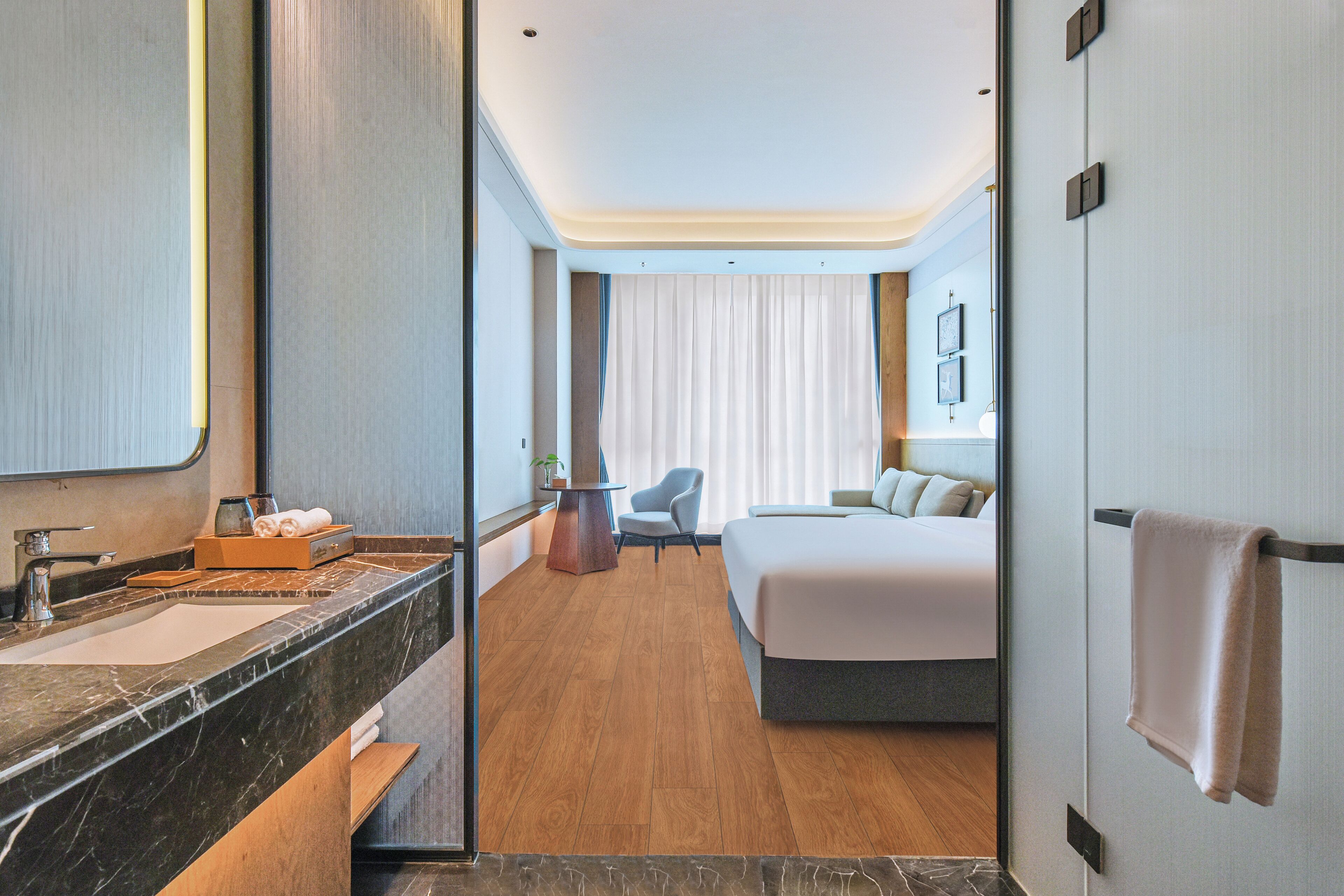 Une chambre d’hôtel avec une salle de bain en marbre, un lit, une chaise et un bureau.