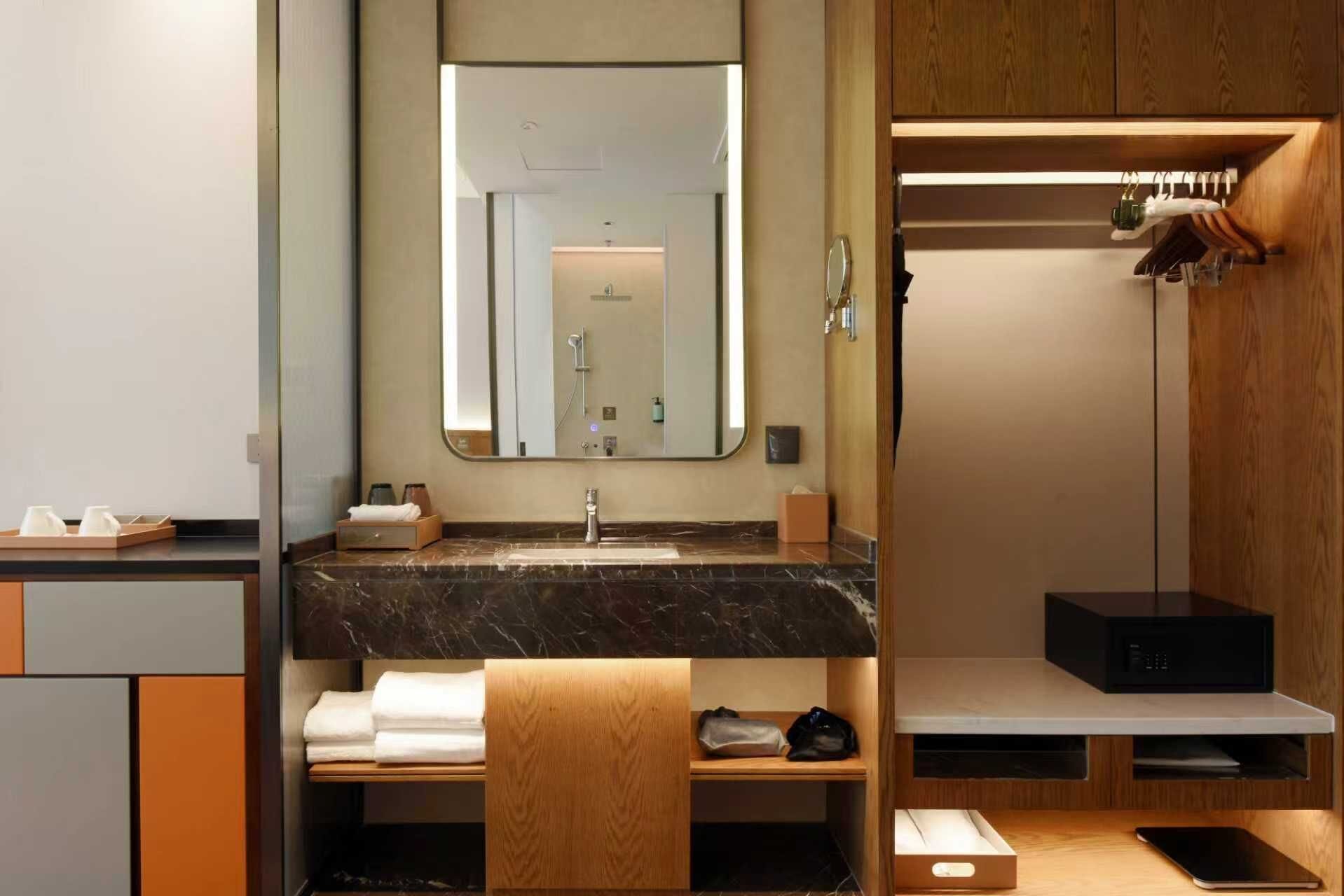 A modern bathroom with a marble sink, a large mirror, a towel rack, and a built-in heater.
