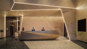 A modern reception desk with a geometric design, two receptionists, and a plant. - Novotel Kunming Yunjin (Kunming)