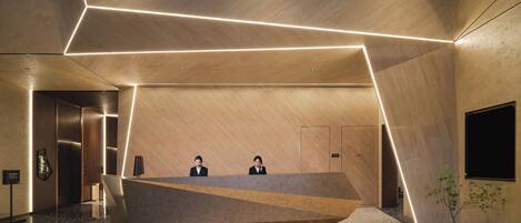 A modern reception desk with a geometric design, two receptionists, and a plant.