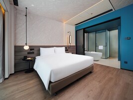 Una moderna camera d'albergo con un letto grande, comodini, una vasca da bagno incassata e un box doccia in vetro.