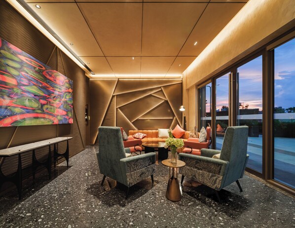 A modern lounge with a geometric patterned wall, a colorful abstract painting, and a seating area with a sofa and two armchairs.