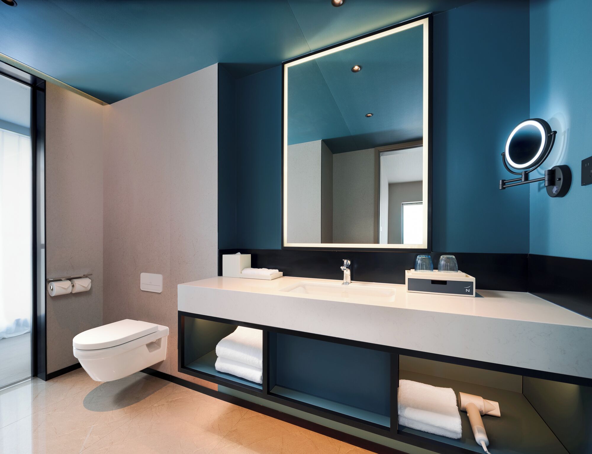 A modern bathroom with a large mirror, a white sink, and a toilet.
