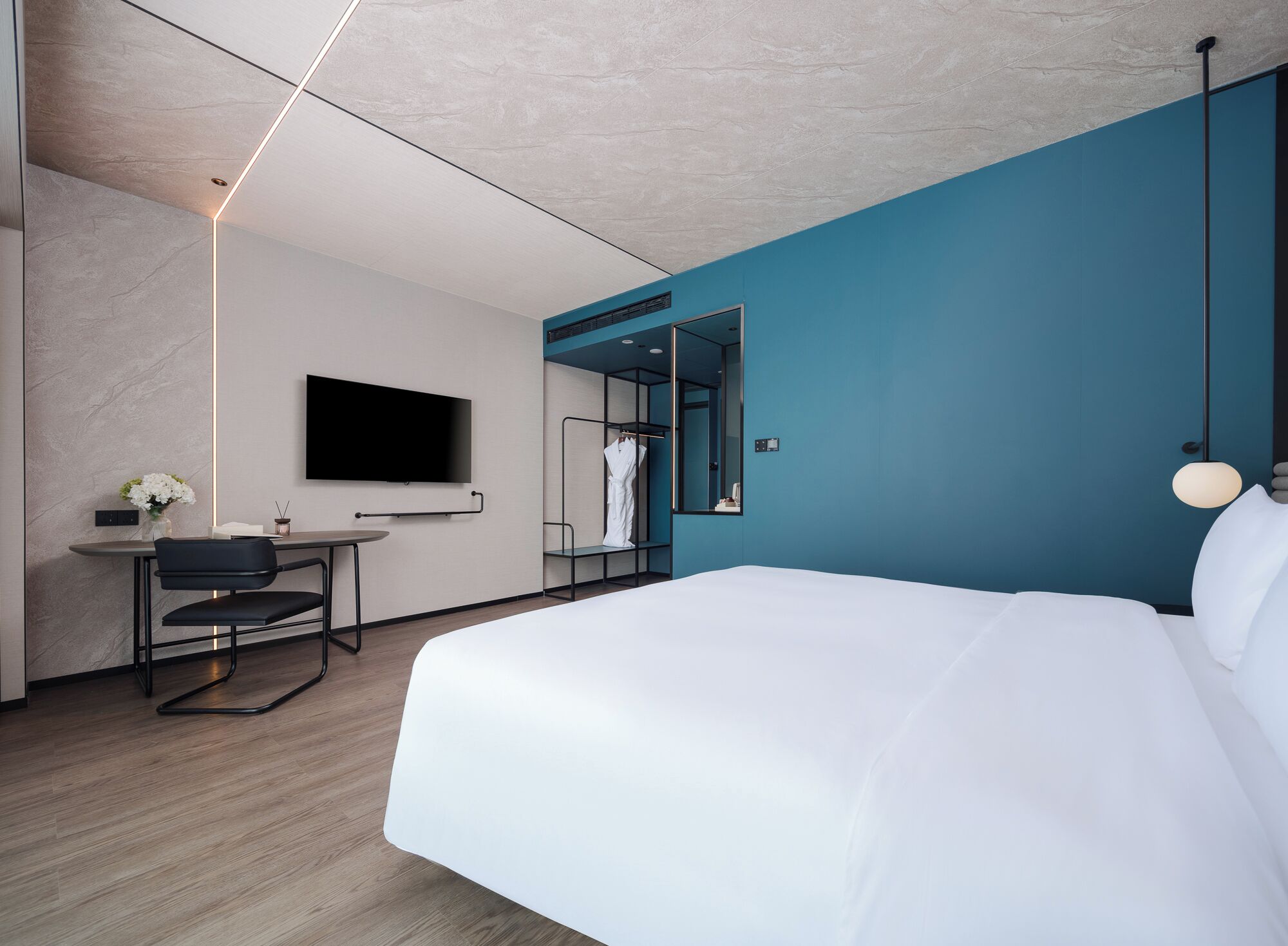 A modern hotel room with a large bed, a desk with a chair, a flat-screen TV mounted on the wall, and a mirror reflecting the room.