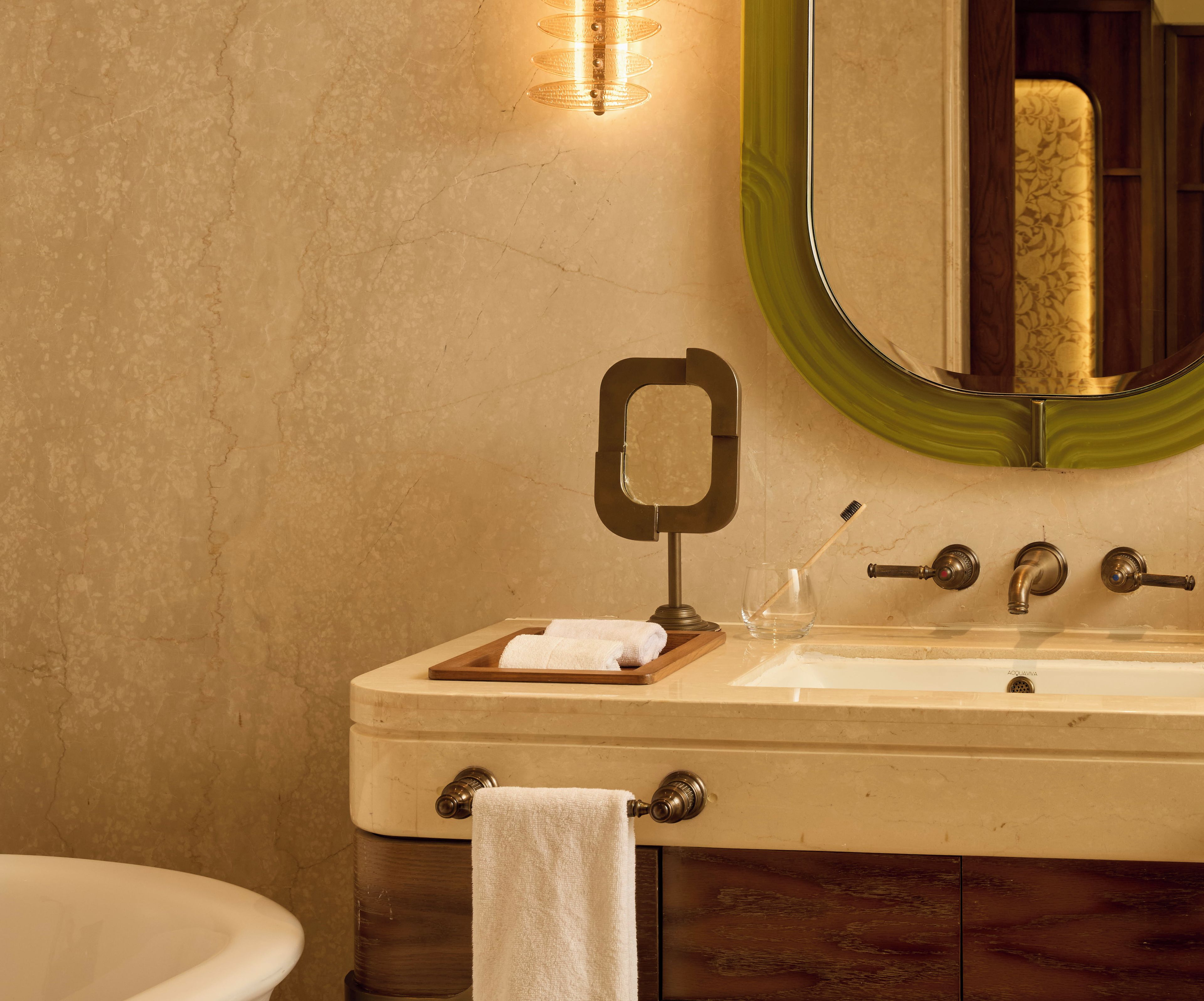 A bathroom with a marble sink, a mirror with a green frame, a towel rack, and a toothbrush holder.