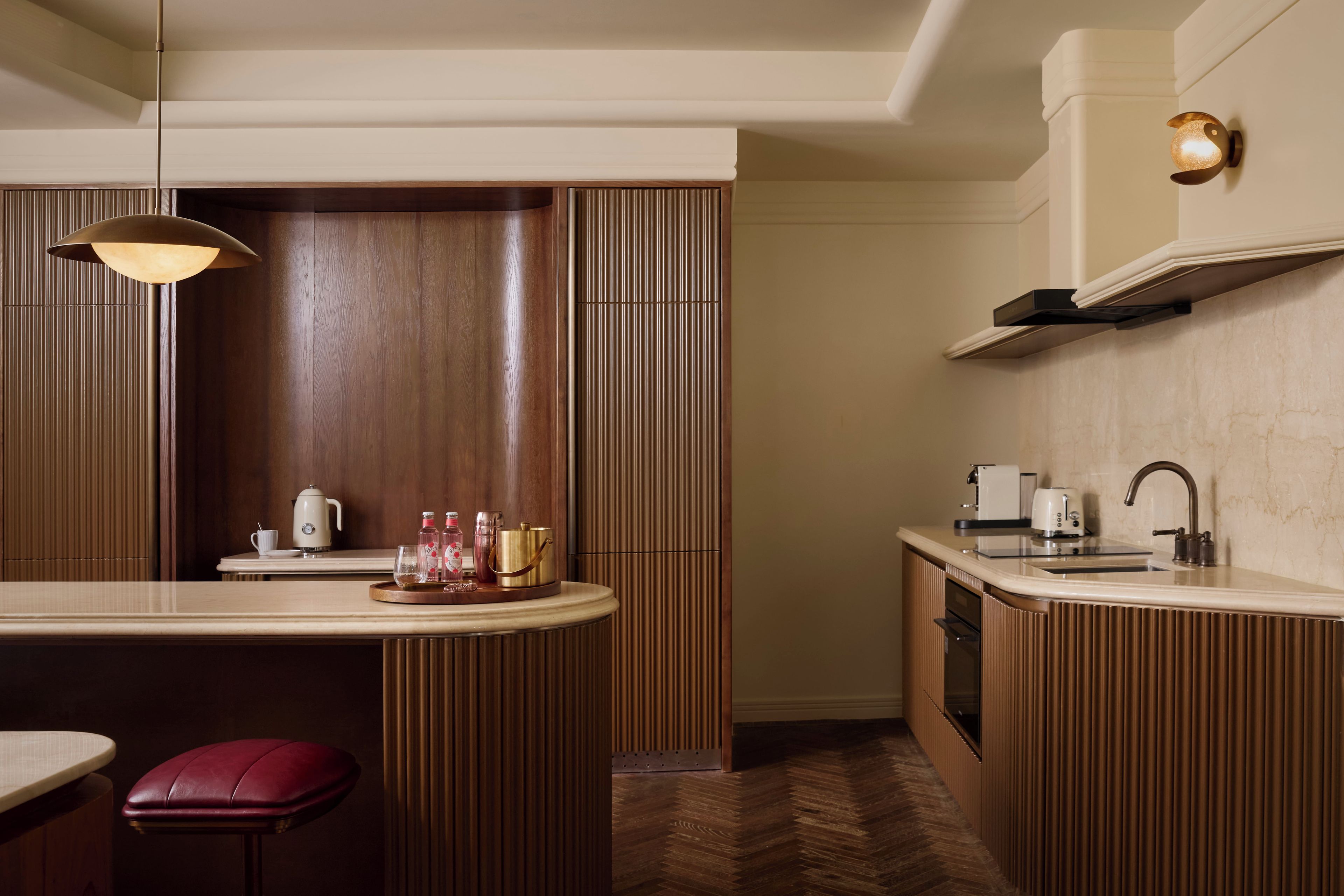 Cocina compacta con diseño de paneles de madera, barra redonda y un taburete rojo.