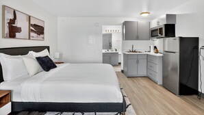 Ein modernes Hotelzimmer mit einem großen Bett, einer Küchenzeile und einem sichtbaren Badezimmer im Hintergrund.