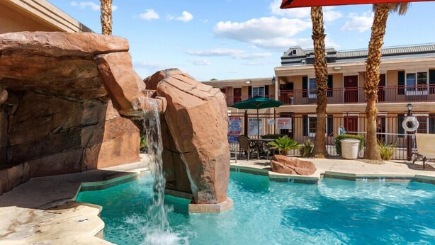 Ein Poolbereich mit Wasserfall, Palmen und einem Gebäude mit Balkonen im Hintergrund.