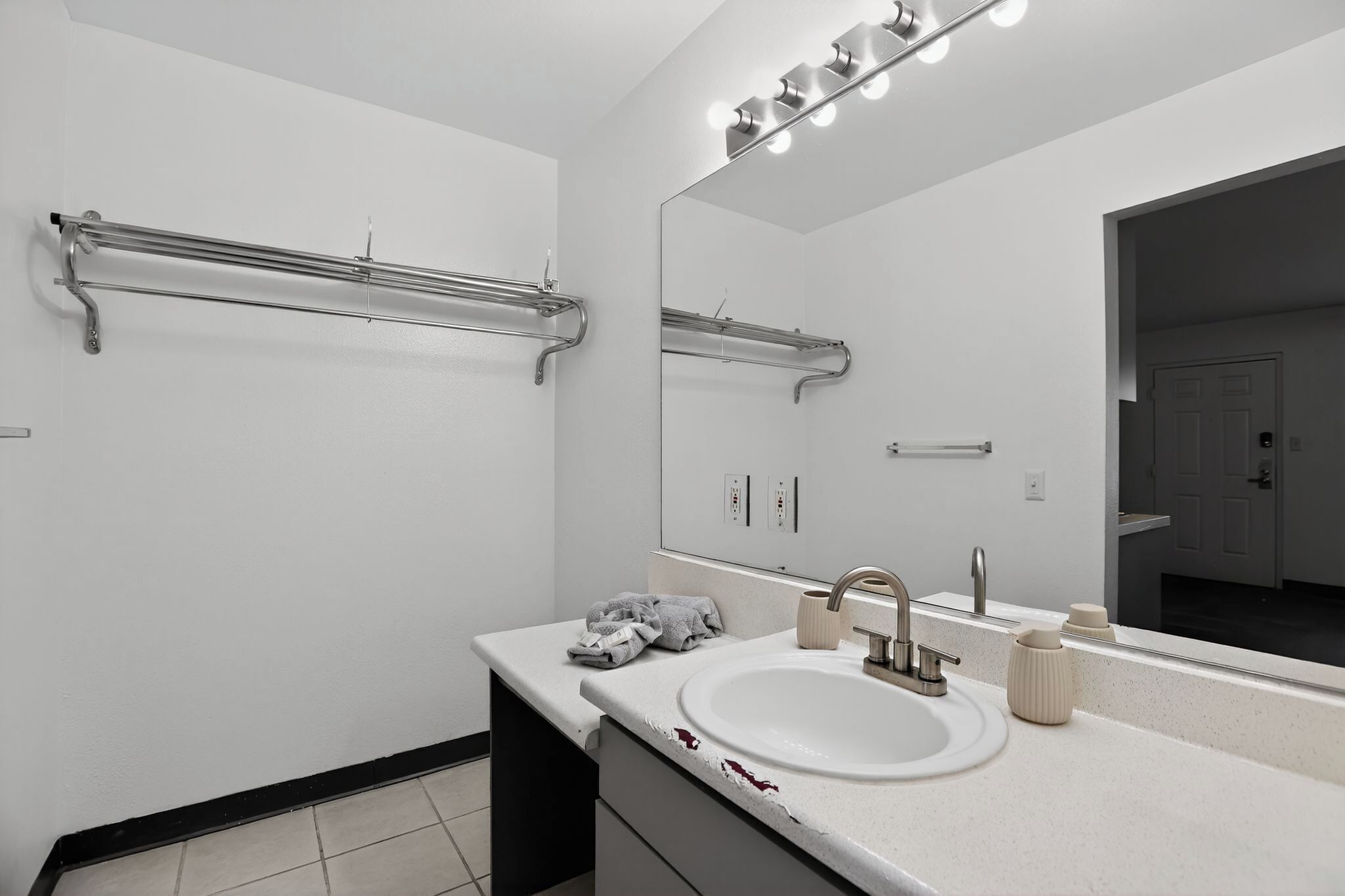 A modern bathroom with a white sink, a large mirror, and a towel rack.