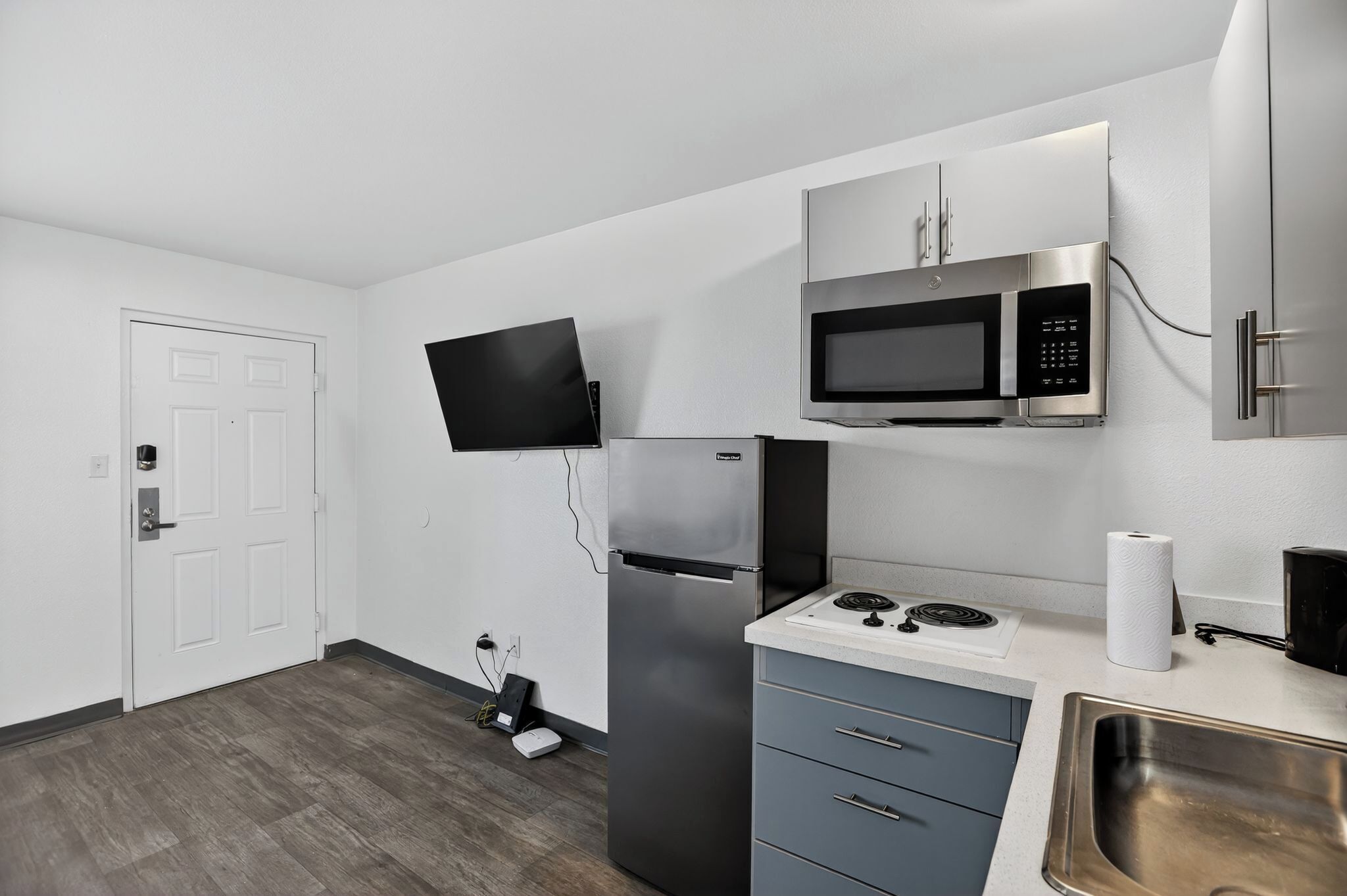 Una cocina compacta con refrigerador, microondas y estufa, televisor de pantalla plana y pileta de acero inoxidable.