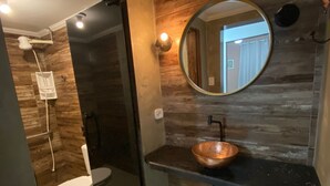 A modern bathroom with a wooden wall, a round mirror, a copper sink, and a glass-enclosed shower. - Romantic chalet for couples in love. (Santa Isabel)