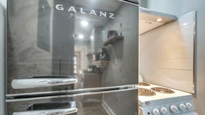 Ein edelstahlfarbener Galanz-Kühlschrank mit Doppeltür steht neben einem weißen Herd mit vier Kochfeldern und einer Bedienkonsole.