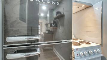 A stainless steel Galanz refrigerator with a double-door design, positioned next to a white stove with four burners and a control panel.