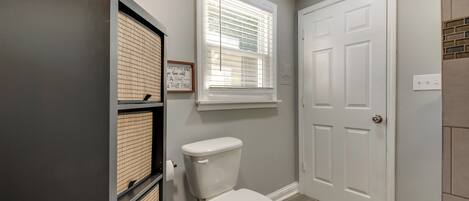 Un baño con inodoro, ventana con persianas, una puerta y un armario.