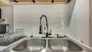 A kitchen with two stainless steel sinks, a black faucet, and a tiled backsplash.