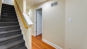 Un escalier dont les marches sont recouvertes de moquette et qui possède une rampe en bois, menant à une porte située en haut.
