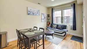 Un coin repas avec une table dressée pour quatre personnes, un canapé avec des coussins, une fenêtre avec des rideaux et des œuvres d’art accrochées au mur.