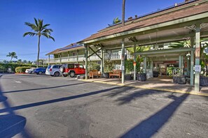 Ein Hotel mit überdachter Außenterrasse, einem Parkplatz mit mehreren Autos und einer Palme im Hintergrund.