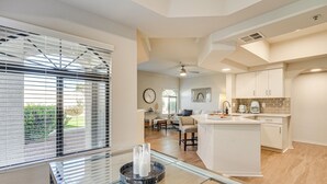 A modern kitchen with white cabinets, a central island, and a dining area with a glass table. - Patio + Community Perks: Stylish Scottsdale Escape (Scottsdale)