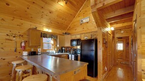 A wooden cabin interior with a kitchen area featuring a refrigerator, microwave, and stove. There are wooden stools at the bar and a sign indicating no smoking. - Log Cabin, Private Hot Tub, Mtn View, Near Dtwn (Gatlinburg)