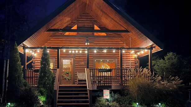 A log cabin with a wooden exterior, a porch with string lights, and a staircase leading to the entrance. - Log Cabin, Private Hot Tub, Mtn View, Near Dtwn (Gatlinburg)