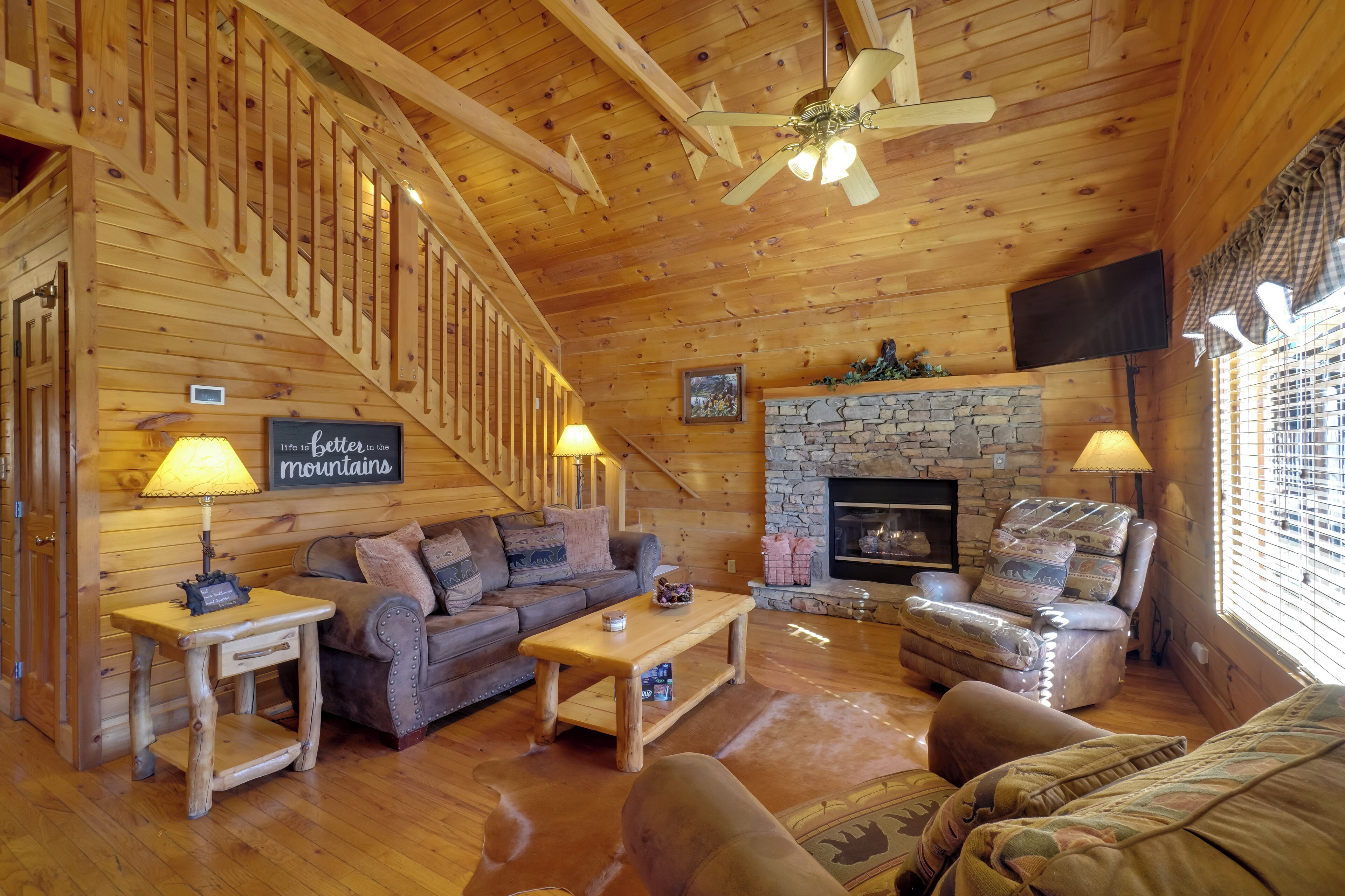 L’intérieur d’un chalet confortable, avec des murs en rondins de bois, une cheminée en pierre, des meubles en bois et un escalier.