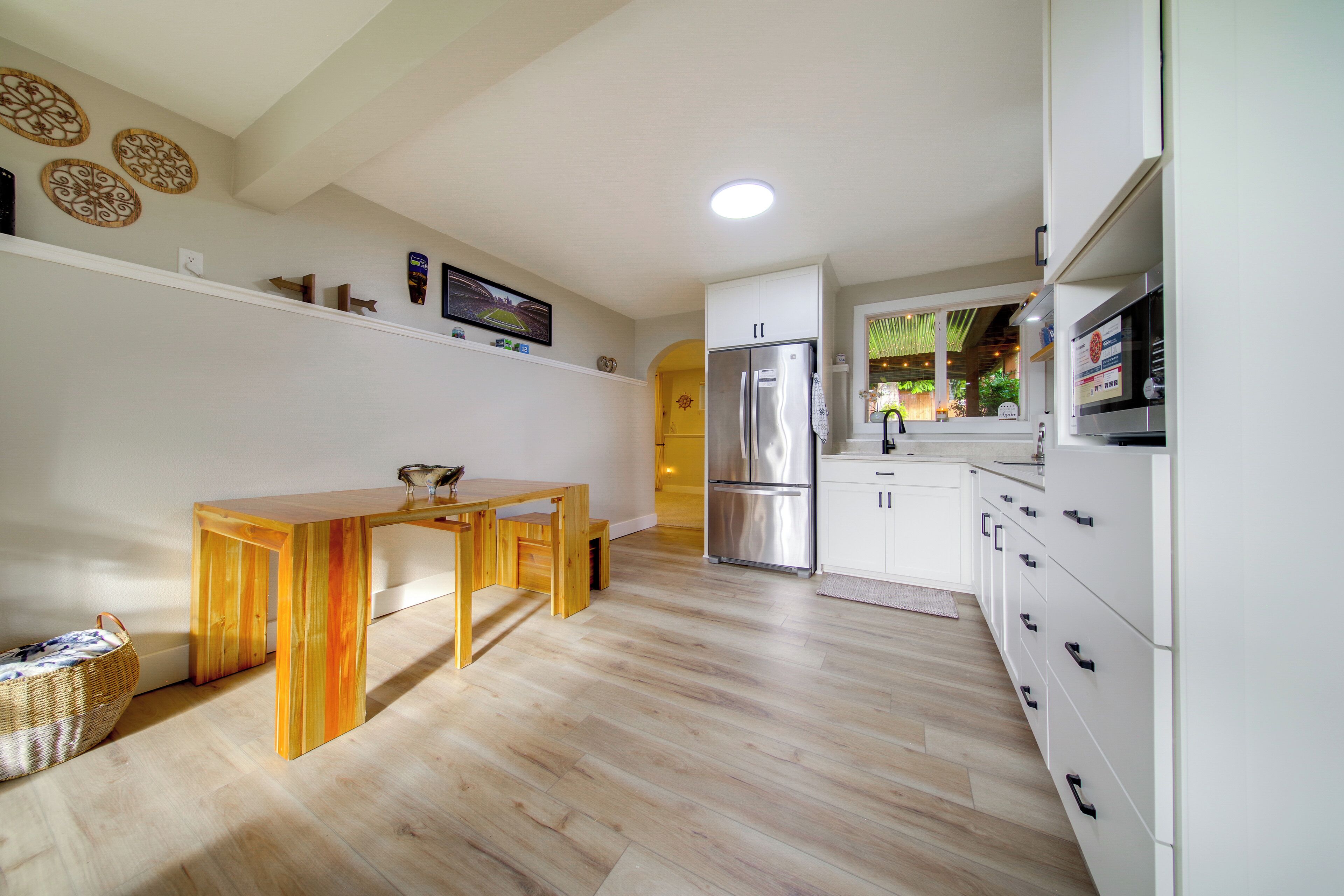 A modern kitchen with wooden flooring, white cabinets, a stainless steel refrigerator, and a wooden dining table.