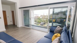 A modern living room with a blue sofa set, a glass door leading to a balcony, and a wooden floor. - Milkwood Villa (Carmarthen)