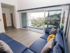 Un salón moderno con un sofá azul, un ventanal de vidrio que da a un balcón y suelo de madera.