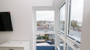 A room with a white dresser, a window with a view of a cityscape, and a blue railing. - Milkwood Villa (Carmarthen)