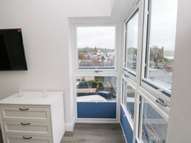 Una habitación con un aparador blanco, una ventana con vistas a un paisaje urbano y una barandilla azul.